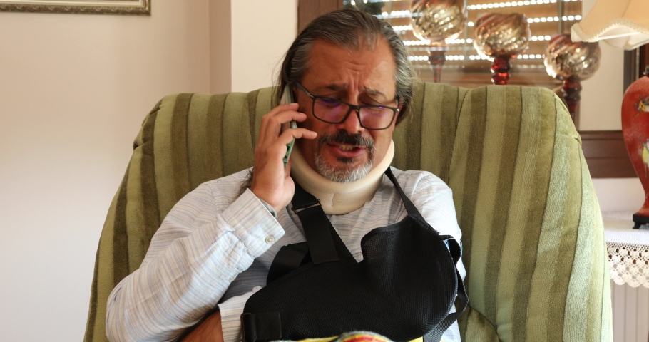 Painful man with neck and arm brace calling doctor with smartphone. Royalty-Free Stock Footage #1061183419