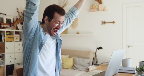Happy young businessman in glasses feeling excited reading email with good news on computer, received bank loan approval, money payment or celebrating personal professional success, good luck concept.