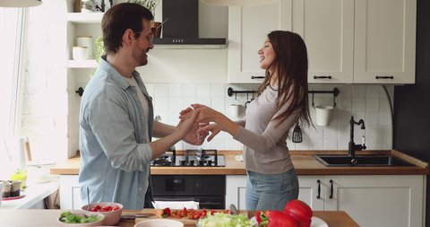 Smiling young handsome man twisting beautiful wife, dancing together in modern kitchen. Happy loving affectionate married family couple enjoying home dating weekend time, distracted form cooking.