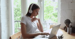 Focused young woman in headphones working on computer, preparing marketing data research results or web surfing information. Skilled millennial girl studying online, listening audio lecture at home.
