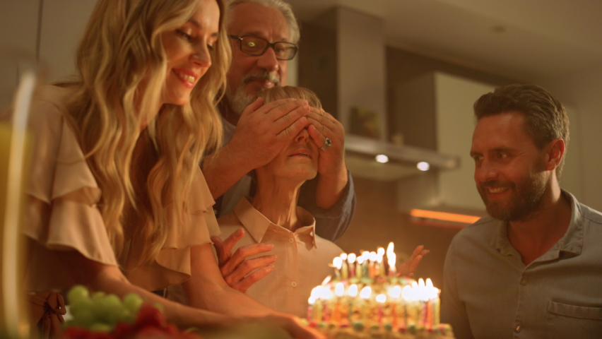 Big family celebrating grandmother birthday at home. Senior man closing woman eyes for surprise. Excited mature woman looking at cake with burning candles. Happy family clapping hands together Royalty-Free Stock Footage #1061190691