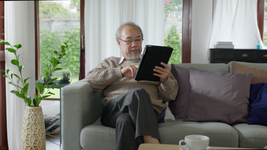 Candid of old senior asian grandparent play and watch with kid grandchildren with technology on computer tablet at home in bonding relationship in family. Young girl hug older man from back. Royalty-Free Stock Footage #1061194042