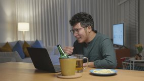 Zoom in : Attractive young happy asian man enjoy relax night party event online celebration festive with friends at house clinking beer with glass and bottle toasting drinking via video call.