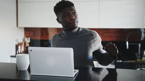 young african american black man working on laptop in his appartment stretching and looking through the window. High quality 4k footage