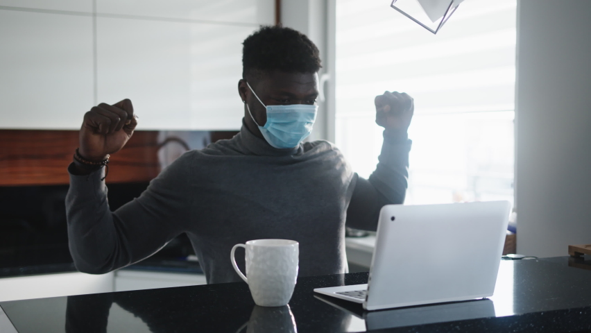 Young african american black man stretching while working on laptop in his appartment with face mask on. High quality 4k footage | Shutterstock HD Video #1061194597