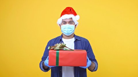A man is celebrating New Year and Christmas. He wears a Christmas hat and delivers the gift box to his loved ones. He wears a mask and gloves to protect against the coronavirus. 4K Resolution.