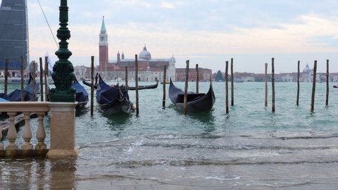 Venezia, Italy, 18 october, 2020 - High tide sweeping upon the steps leading to the lagoon in front of famous Piazza San Marco square, with docked gondolas floating and sailboats in the background. 