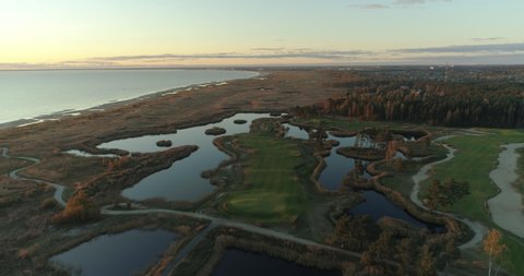 Golf course and reed field on sea coast at sunset aerial view