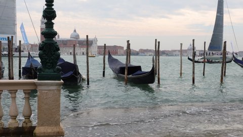 Venezia, Italy, 18 october, 2020 - High tide sweeping upon the steps leading to the lagoon in front of famous Piazza San Marco square, with docked gondolas floating and sailboats in the background. 