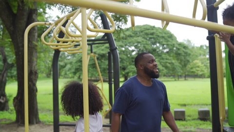 Happy affectionate mixed race family. African man father carrying little daughter playing at playground in the park. Dad and two child girl enjoy and having fun together in outdoor weekend vacation.