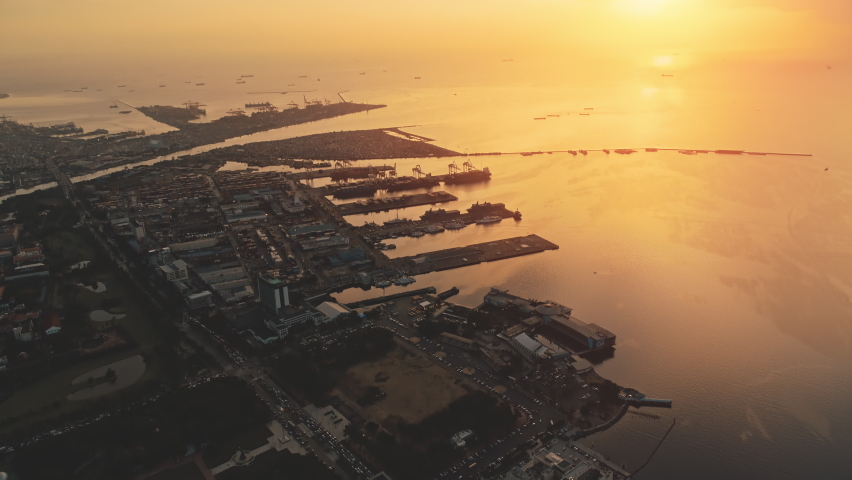 Sunset over pier town at ocean bay aerial. Amazing sun set light at seascape with marina on shore. Ships, yachts and boats stay at port on serene sea water. Philippines harbor town Manila cityscape