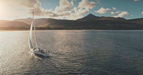 Sailing yacht in wind waves at Arran Island sea bay in Scotland. Amazing seascape at Brodick port city. Lonely sail boar race at sun shine with fluffy clouds. Serene water scape and transportation