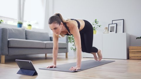 Happy woman practicing climber exercises at home watching workout routine on digital tablet