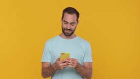Fun confident charismatic happy bearded young man in basic casual blue t-shirt posing doing selfie shot on mobile cell phone video call isolated on yellow background studio. People lifestyle concept