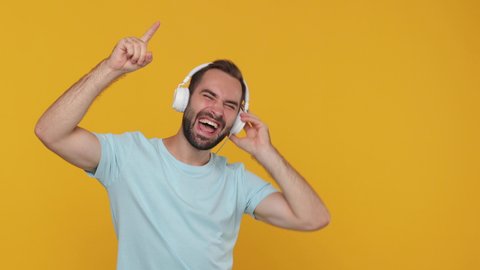 Handsome excited young man guy 20s years old in basic casual blue t-shirt relax enjoy dance have fun listen good cool music in headphones isolated on yellow background studio. People lifestyle concept