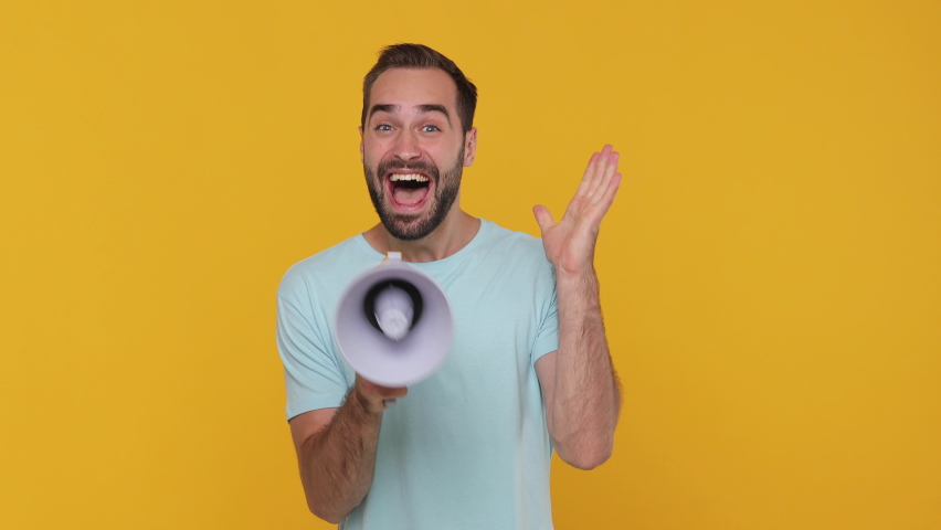 Funny excited young man 20s years old in basic casual blue t-shirt isolated on yellow background studio. People lifestyle concept. Looking camera scream in megaphone announces discounts sale Hurry up