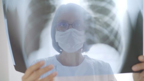 4K Female Doctor wearing eyeglasses and face mask examining X-ray scan of patient. Health service concept, surgery and serious illness concept.