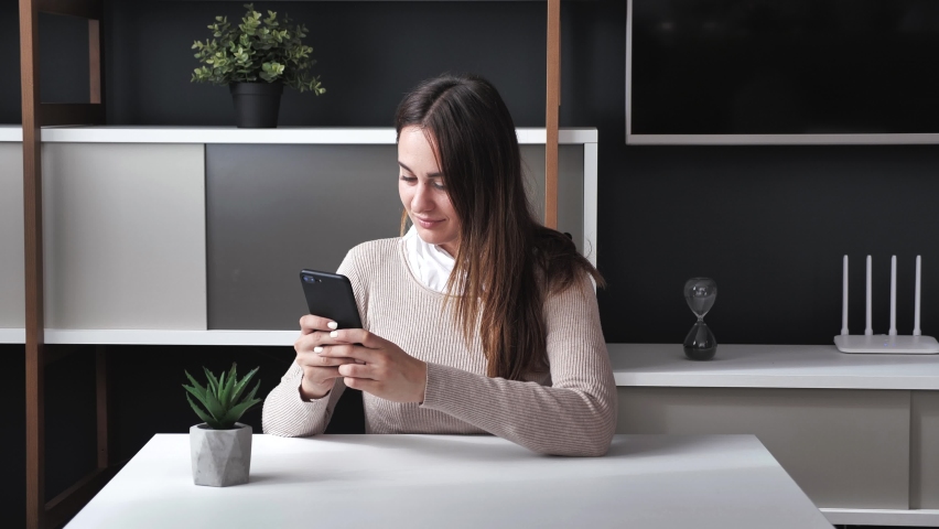 Millennial young woman spending time at office with cell gadget technology. Relaxed lady using smart phone surfing social media, checking news, playing mobile games or texting messages at modern Royalty-Free Stock Footage #1061222572