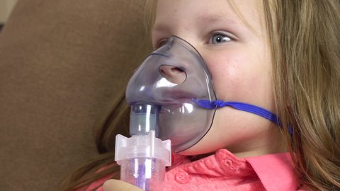 A little girl makes inhalation with a nebulizer while lying in bed.Child is sick bronchitis and breathes through an inhaler in home.4k.