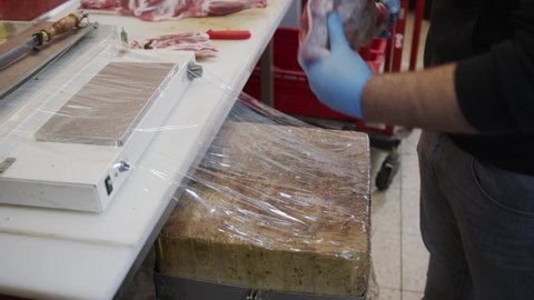 Worker in gloves packs fresh meat in plastic film. Packing of meat. Fresh meat in supermarket.