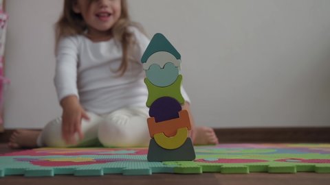 Childhood, family, insulation concept - One cute small happy child build wooden pyramid sitting on floor colored soft mat puzzle. kid girl playing alone educational games for motor skills at home.