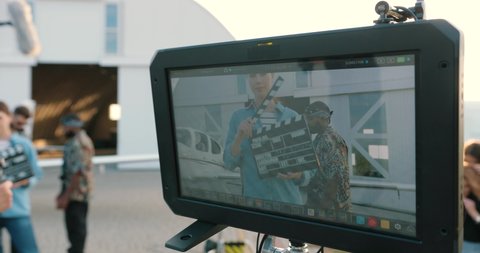 Camera approaching mixed-race male actors standing outdoor on set near hangar. Female making scene with clapperboard. Caucasian man giving money to African American guy. Close up concept
