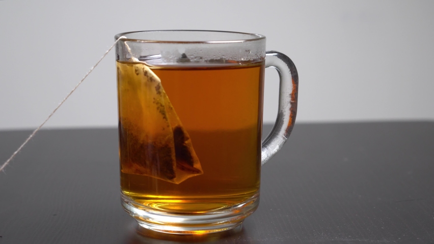 Boiling water is poured into a glass cup with a disposable tea bag on white bachground. Hot cup of black tea.
