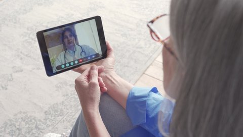 Over shoulder view of older elderly woman patient meeting virtual doctor using tablet at home. Online telemedicine visit. Seniors ehealth, telehealth medical consultation, tele medicine video call.