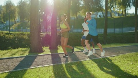Attractive multi-ethnic youth performing running cardio workout together outdoors. Three best friends jogging in open nature enjoying active lifestyle. Sports people. Fitness.