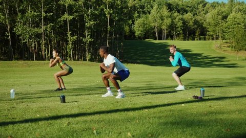 Diverse attractive fitness friends performing aerobics jumping exercises warming-up together smiling enjoying group training outside in the fresh air. Sports team concept.
