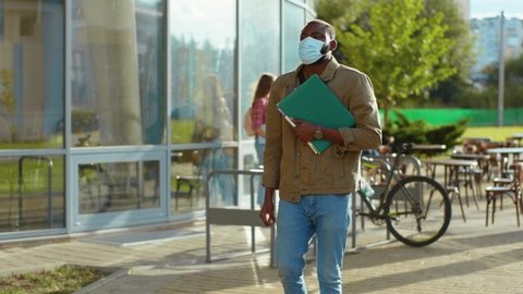 Two multi-race young male students wearing face masks meeting with elbow bums communicating standing near campus. University. Education on quarantine. Personal safety.