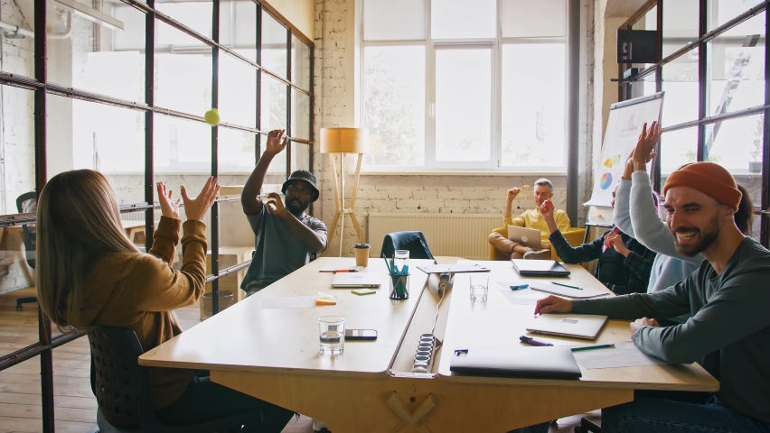 Informal meeting in office. Group of young coworkers throwing tennis ball to each other, sitting at desk, slow motion | Shutterstock HD Video #1061233705