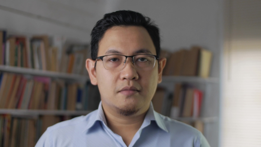 Portrait of cheerful Asian male librarian, looking at camera and smiling, man standing against books in library Royalty-Free Stock Footage #1061233765