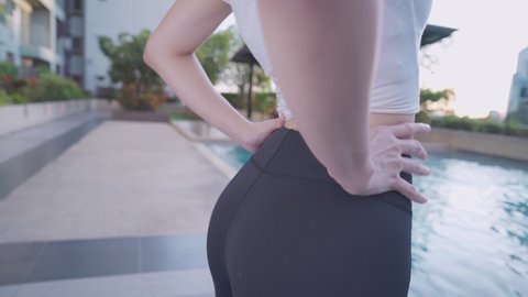fit young female hurting her back lower back pain, hip waist spine injury, self massage stomp standing outside building, low camera angle close up female back ache, woman in sportwear during exercise