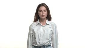 Close-up of attractive brunette woman in white collar shirt, looking confused, clip her eyes at something unbelievable, standing over studio background