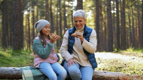picking season, leisure and people concept - grandmother and granddaughter having picnic and eating pie in autumn forest