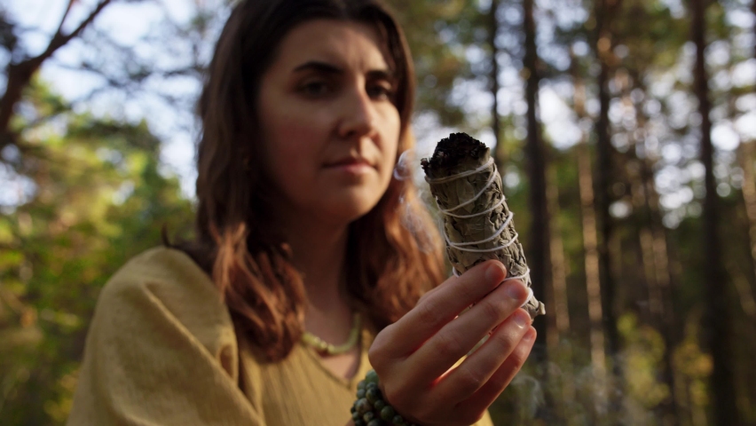 Occult science and supernatural concept - young woman or witch with smoking white sage performing magic ritual in forest | Shutterstock HD Video #1061244358