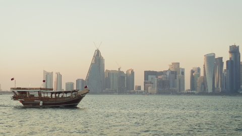 Doha, Qatar- October 24 2020: Doha skyline afternoon left to right panning shot showing Dhow with Qatar flags in the Arabic gulf in foreground and Doha skyline in background
