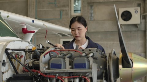 Young asian female aviation maintenance engineer doing a pre flight checkup or maintenance on a small engine aircraft in hangar. Transportation and Technology concept.