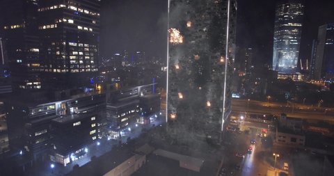 Building destroyed on fire with smoke at night- Aerial view 
Drone footage, Modern High tower Skyscraper with debris and Rescue vehicles,
Tel aviv, Israel