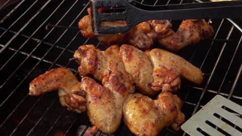Delicious chicken wings are roasting and flipping with the kitchen tongs on the grill grid