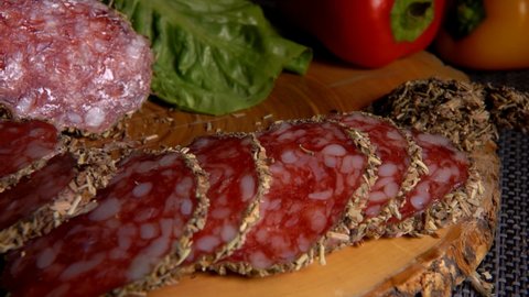 Panorama of delicious dry sausage in herbs taken from a wooden board with a fork on the background of pepper and greenery