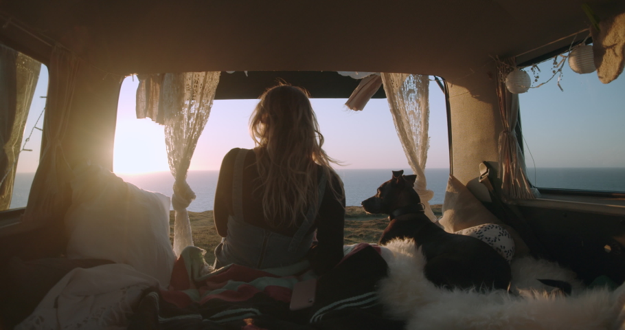 Woman and her dog watching the sunset from the trunk of their van in Devon, England, UK