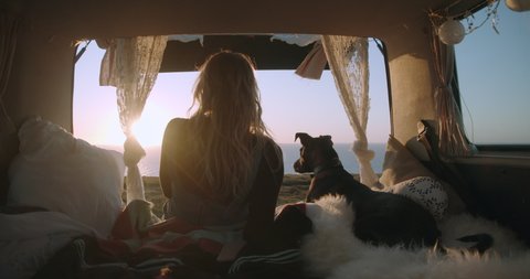 Woman and her dog watching the sunset from the trunk of their van in Devon, England, UK