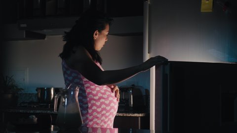 Latin pregnant woman eating sweet food late at night, hungry hispanic girl with cravings during pregnancy, opening refrigerator and eating cake at home