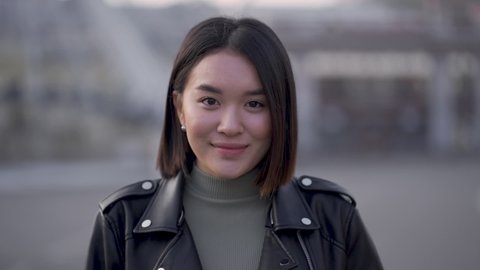 Portrait of young pretty asian woman smiling and looking at camera outdoors. Front view.