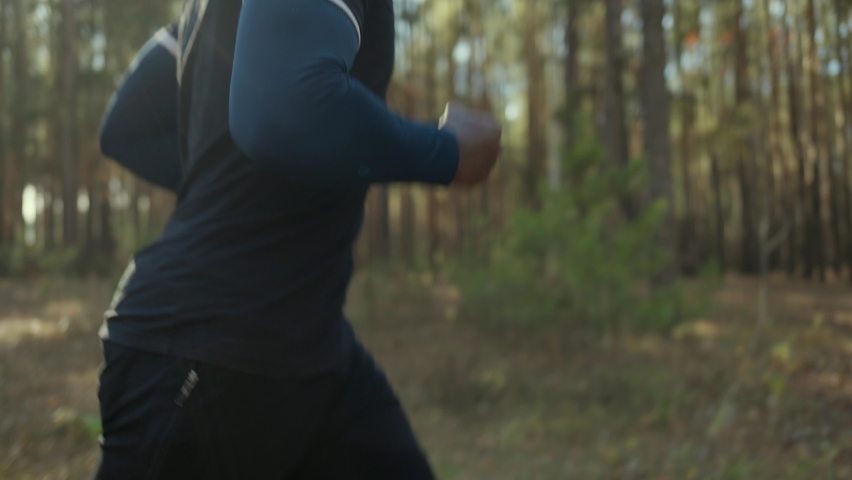 Young fit African American male jogging on a forest road.