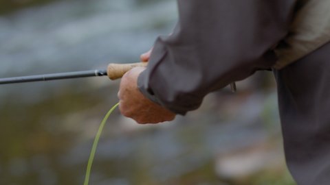 Fly fisherman fishing with spinning
Male hands twist the spinning reel fly while fishing. 
Fisherman catches fish in slow motion
Fly Fishing Reel with river water on background, close up.
 