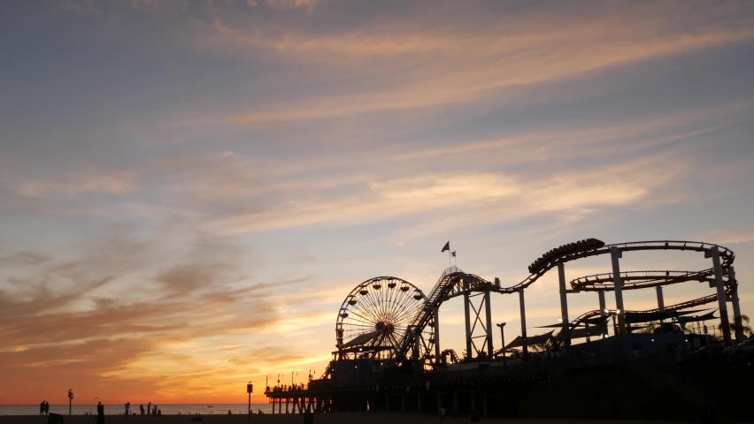 Classic ferris wheel, amusement park on pier in Santa Monica pacific ocean beach resort. Summertime California aesthetic, iconic view, symbol of Los Angeles, CA USA. Sunset golden sky and attractions. Royalty-Free Stock Footage #1061260819