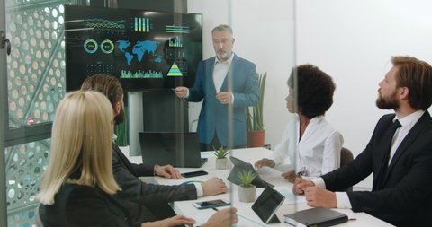 Likable serious confident bearded leader of group of mixed race ecological experts doing presentation on digital whiteboard during joint meeting in boardroom